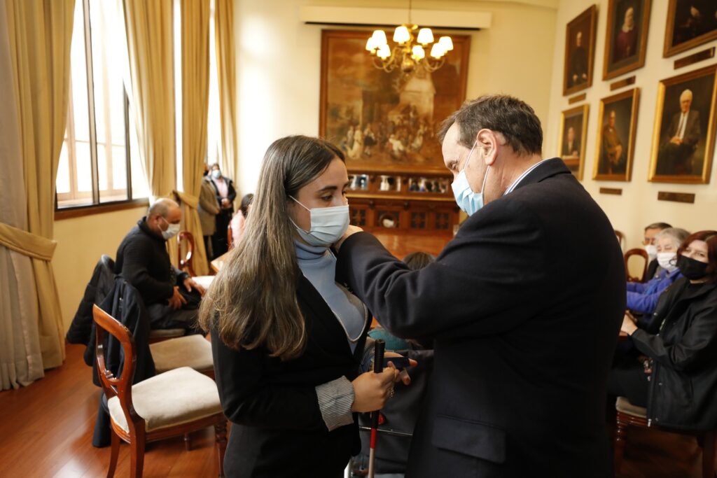 El Rector UC otorgando una piocha de la universidad a Sara Lara, una de las estudiantes que realizará un intercambio bilateral por la vía equidad de vacantes.